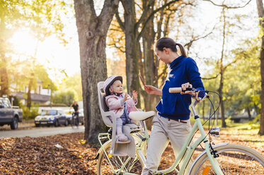 Mother and daughter riding bicycle, baby wearing helmet sitting in children's seat - DIGF03177