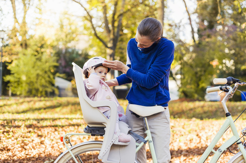 Mother and daughter riding bicycle, baby wearing helmet sitting in children's seat stock photo