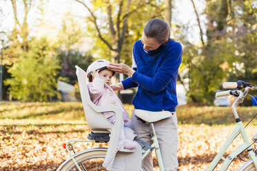 Mutter und Tochter fahren Fahrrad, das Baby trägt einen Helm und sitzt im Kindersitz - DIGF03178