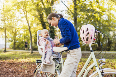 Mother and daughter riding bicycle, baby wearing helmet sitting in children's seat - DIGF03179