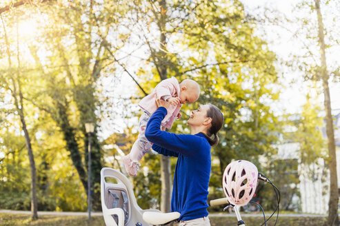 Mutter und Tochter fahren Fahrrad, heben das Baby aus dem Kindersitz - DIGF03180