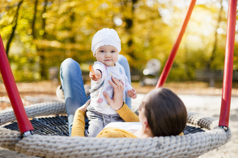 Porträt eines kleinen Mädchens, das sich mit seiner Mutter auf einer Schaukel im Herbst entspannt, lizenzfreies Stockfoto