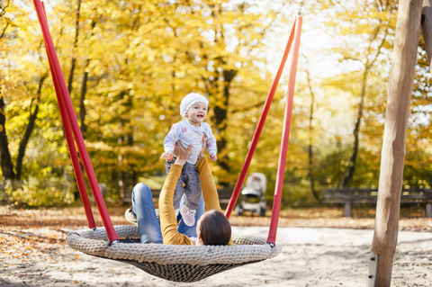 Glückliches kleines Mädchen entspannt sich mit ihrer Mutter auf einer Schaukel im Herbst, lizenzfreies Stockfoto