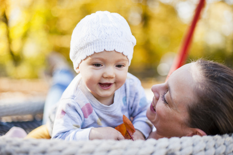 Porträt eines glücklichen kleinen Mädchens, das sich mit seiner Mutter auf einer Schaukel im Herbst entspannt, lizenzfreies Stockfoto