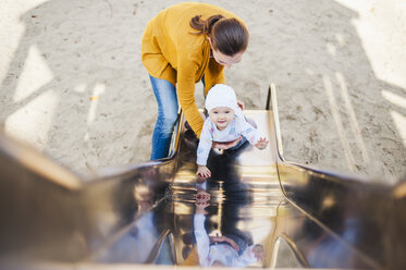 Smiling baby girl on shute on playground being held by her mother - DIGF03196