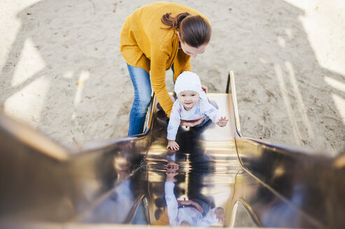 Lächelndes kleines Mädchen auf dem Spielplatz, das von seiner Mutter gehalten wird - DIGF03196