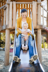 Glückliches kleines Mädchen, das mit seiner Mutter auf einer Rutsche auf dem Spielplatz sitzt - DIGF03199