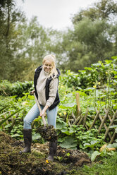Lächelnde junge Frau bei der Arbeit mit dem Spaten im Garten - JOSF01880