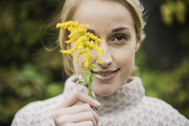 Porträt einer lächelnden jungen Frau, die eine Wildblume hält - JOSF01888