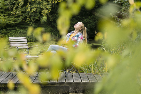 Junge Frau entspannt sich auf einem Steg im Garten, lizenzfreies Stockfoto