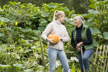 Glückliche junge Frau mit ihrer Großmutter, die einen Kürbis im Garten hält - JOSF01895