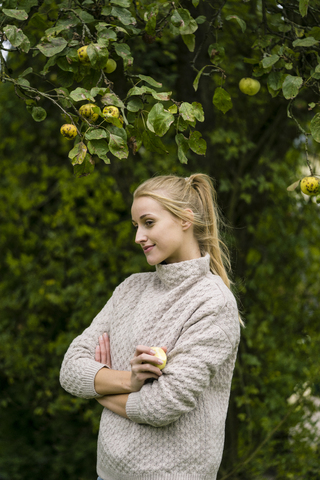 Lächelnde junge Frau am Apfelbaum im Garten, lizenzfreies Stockfoto