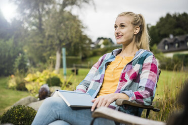 Lächelnde junge Frau mit Buch entspannt im Garten - JOSF01901