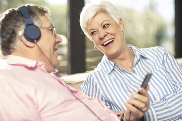 Glückliches älteres Paar mit Handy und Kopfhörern auf der Couch zu Hause - ZEF14730