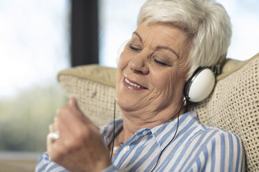 Lächelnde ältere Frau mit Kopfhörern beim Musikhören zu Hause - ZEF14732