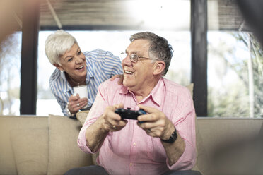 Happy senior man with wife playing video game on couch at home - ZEF14733