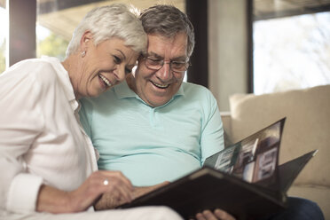 Happy senior couple sitting on couch looking at photo album - ZEF14737