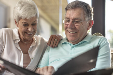 Happy senior couple sitting on couch looking at photo album - ZEF14738