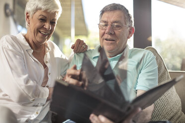 Happy senior couple sitting on couch looking at photo album - ZEF14739