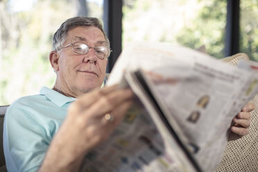Senior man sitting on couch reading newspaper - ZEF14740