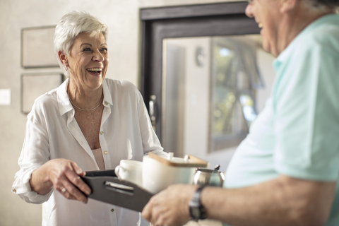 Glückliche ältere Frau serviert ihrem Mann Kaffee auf einem Tablett, lizenzfreies Stockfoto