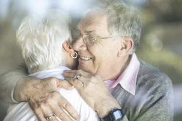 Happy senior couple hugging behind windowpane - ZEF14767