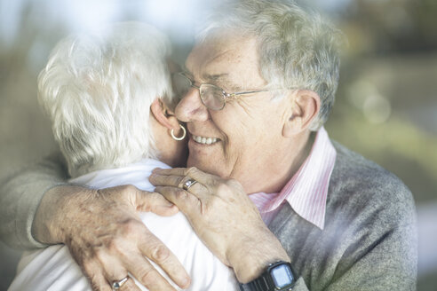 Glückliches älteres Paar, das sich hinter einer Fensterscheibe umarmt - ZEF14767
