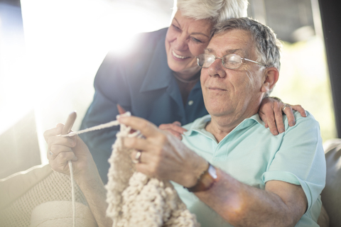 Glückliches Seniorenpaar auf der Couch zu Hause beim Stricken, lizenzfreies Stockfoto