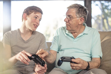 Grandfather and grandson playing video game on couch at home - ZEF14778