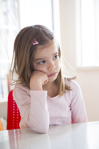 Portrait of sad little girl at table stock photo
