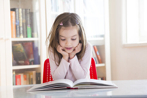 Portrait of little girl at table reading a book - LVF06418