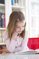 Portrait of smiling little girl at table reading a book - LVF06419