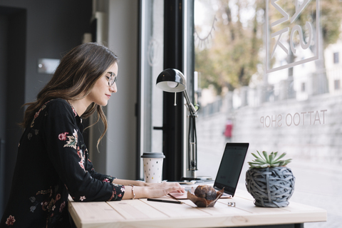 Frau arbeitet am Laptop am Schreibtisch im Tattoo-Studio, lizenzfreies Stockfoto