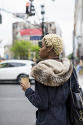 USA, New York City, modische junge Frau mit Kaffee zum Mitnehmen wartet am Straßenrand - MAUF01215