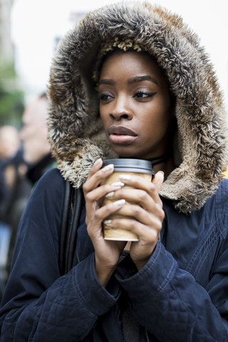 Porträt einer modischen jungen Frau mit Kaffee zum Mitnehmen und Kapuzenjacke, lizenzfreies Stockfoto