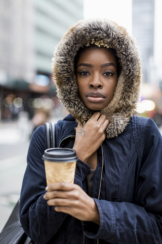 Porträt einer modischen jungen Frau mit Kaffee zum Mitnehmen und Kapuzenjacke, lizenzfreies Stockfoto