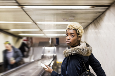 Porträt einer jungen Frau mit Handy auf einem Rolltreppenhaus in einer U-Bahn-Station, lizenzfreies Stockfoto