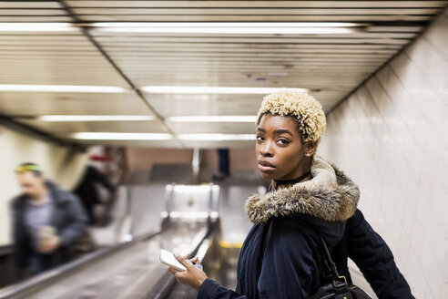 Porträt einer jungen Frau mit Handy auf einem Rolltreppenhaus in einer U-Bahn-Station - MAUF01227