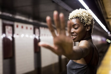 USA, New York City, Porträt einer lachenden Frau auf dem Bahnsteig einer U-Bahn-Station mit erhobener Hand - MAUF01233