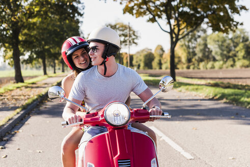 Glückliches junges Paar fährt Motorroller auf der Landstraße - UUF12261