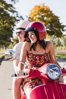 Glückliches junges Paar fährt Motorroller auf der Landstraße - UUF12266