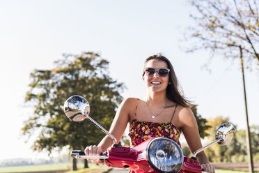 Happy young woman riding motor scooter on country road - UUF12270