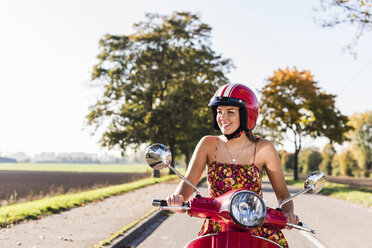 Glückliche junge Frau auf einem Motorroller auf einer Landstraße - UUF12273