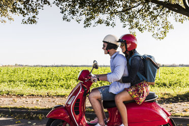Glückliches junges Paar fährt Motorroller mit Rucksack auf dem Rücken - UUF12278