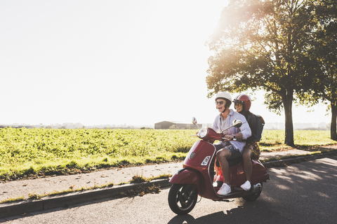 Glückliches junges Paar fährt Motorroller auf der Landstraße, lizenzfreies Stockfoto