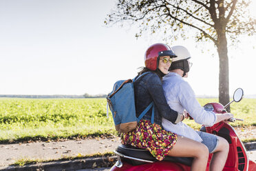 Glückliches junges Paar fährt Motorroller mit Rucksack auf dem Rücken - UUF12280