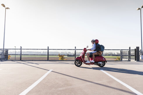 Glückliches junges Paar mit Motorroller auf dem Parkdeck - UUF12281