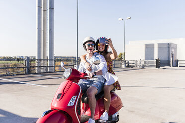 Glückliches junges Paar macht ein Selfie auf einem Motorroller auf einem Parkdeck - UUF12282