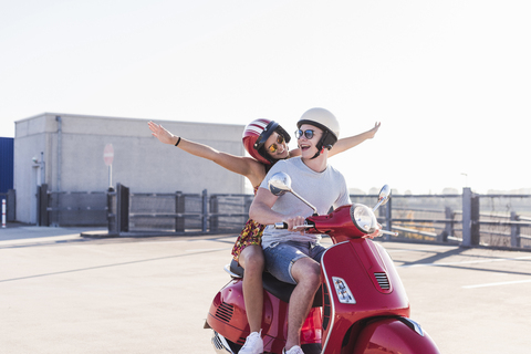 Carefree young couple riding motor scooter on parking level stock photo