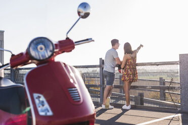 Junges Paar auf einem Parkdeck stehend mit Motorroller im Vordergrund - UUF12290